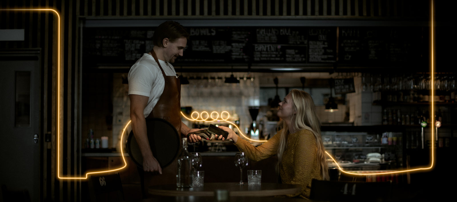 Tjej sitter vid bord och betalar med kort till servitör.